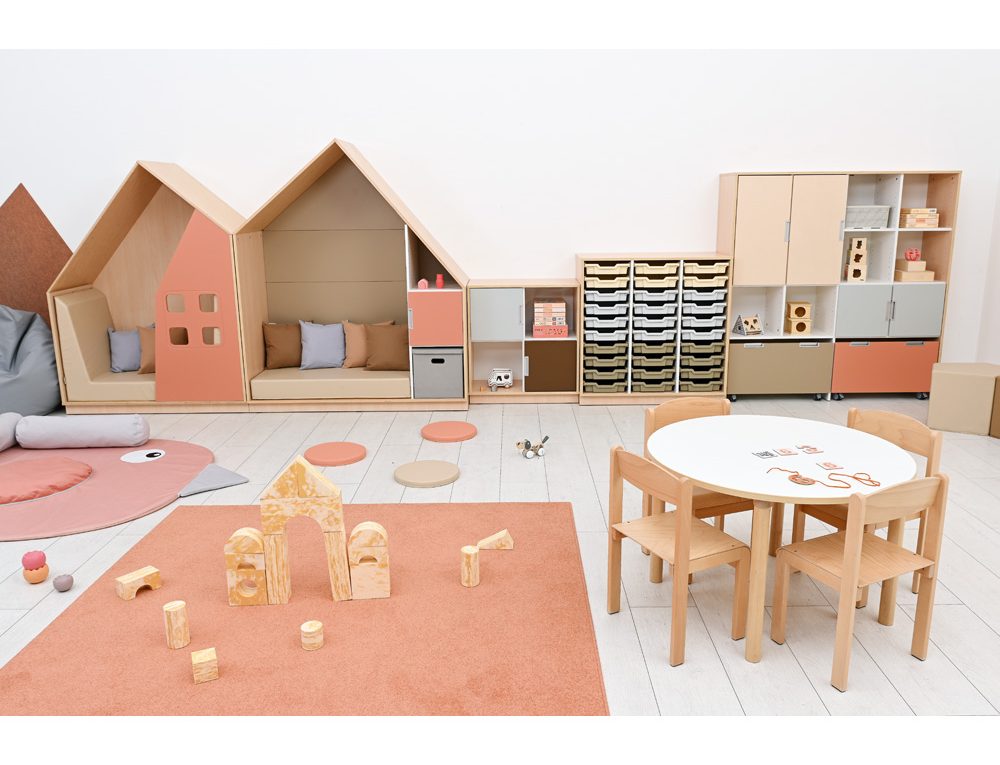 Harmonisk förskolemiljö med trähus, pastellfärgade möbler, lekmatta, bord och stolar för kreativa aktiviteter.