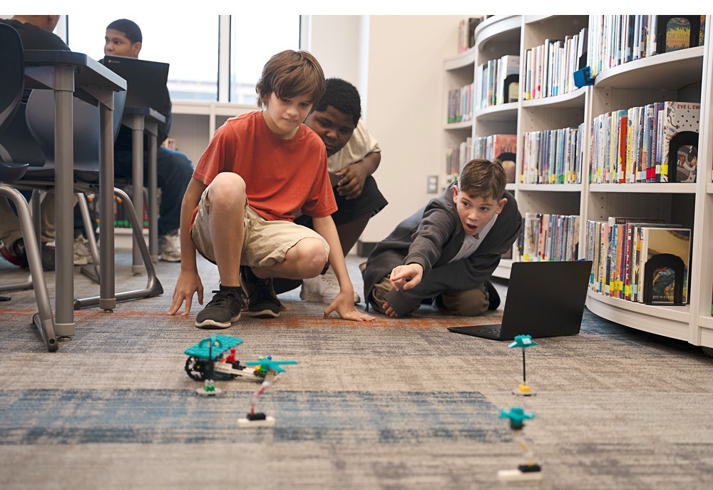 Elever testar en programmerad LEGO® Education-modell tillsammans på golvet under en praktisk STEM-aktivitet.