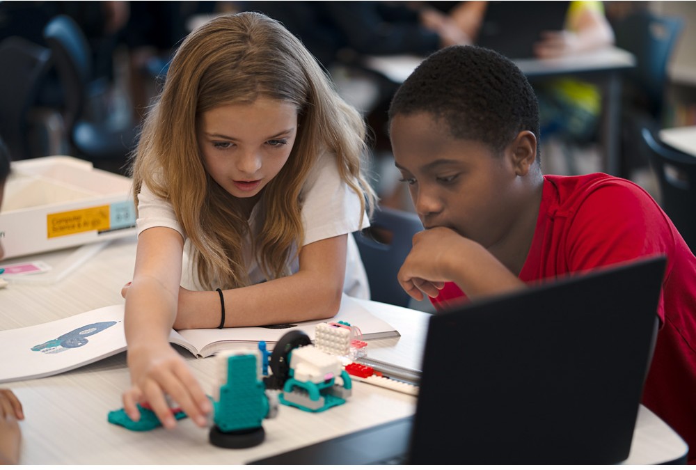 Två elever samarbetar med en LEGO® Education-modell, dator och instruktioner under en praktisk AI-aktivitet.